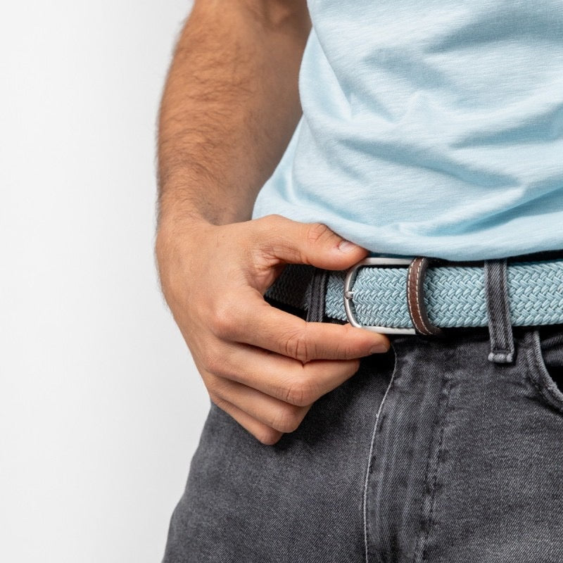 Person adjusting a belt with a light blue shirt and dark jeans on a white background