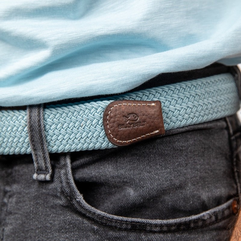 Close-up of a belt with a leather buckle worn by a person, with a light blue shirt and dark pants.