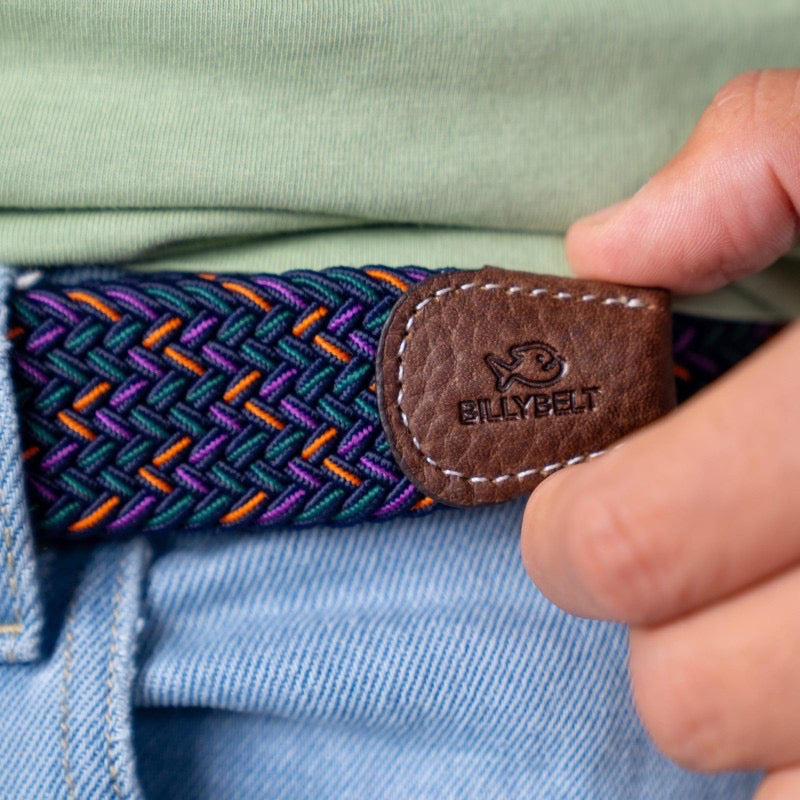 Close-up of a colorful belt with a brown leather patch and 'BILLYBELT' logo, worn on a light blue shirt.