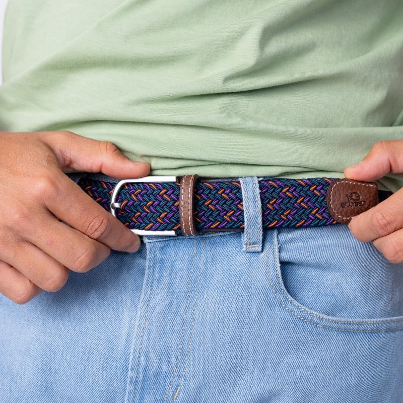 Person wearing a patterned belt with a visible brand logo, holding it with both hands.