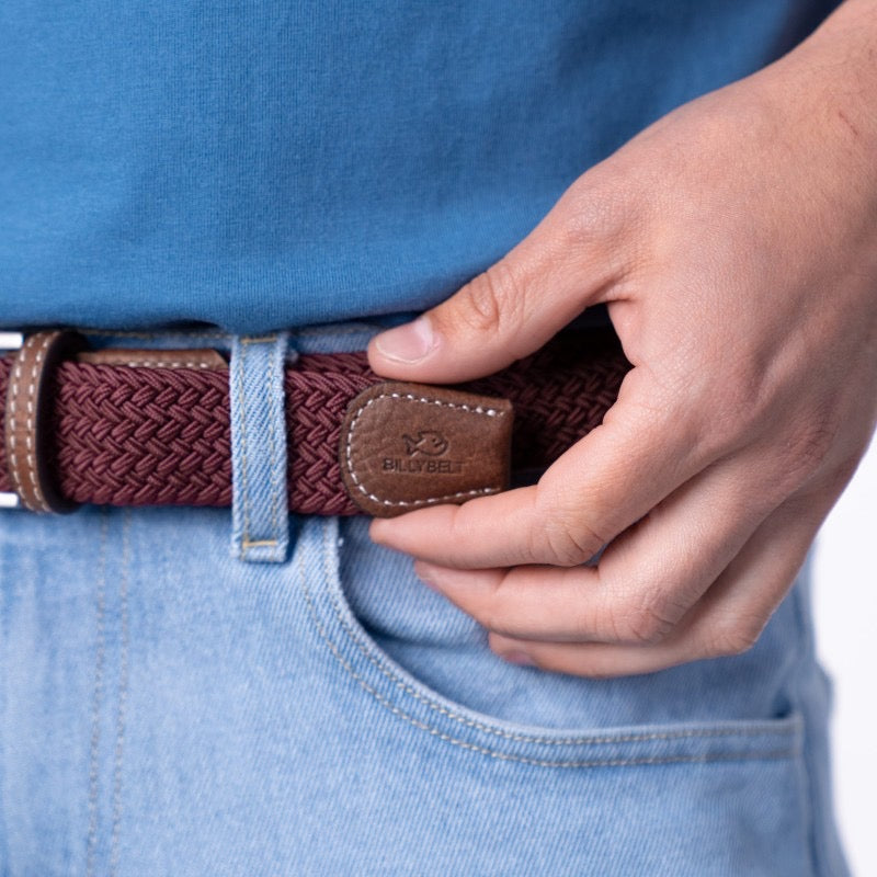 Person adjusting a red woven belt on blue jeans