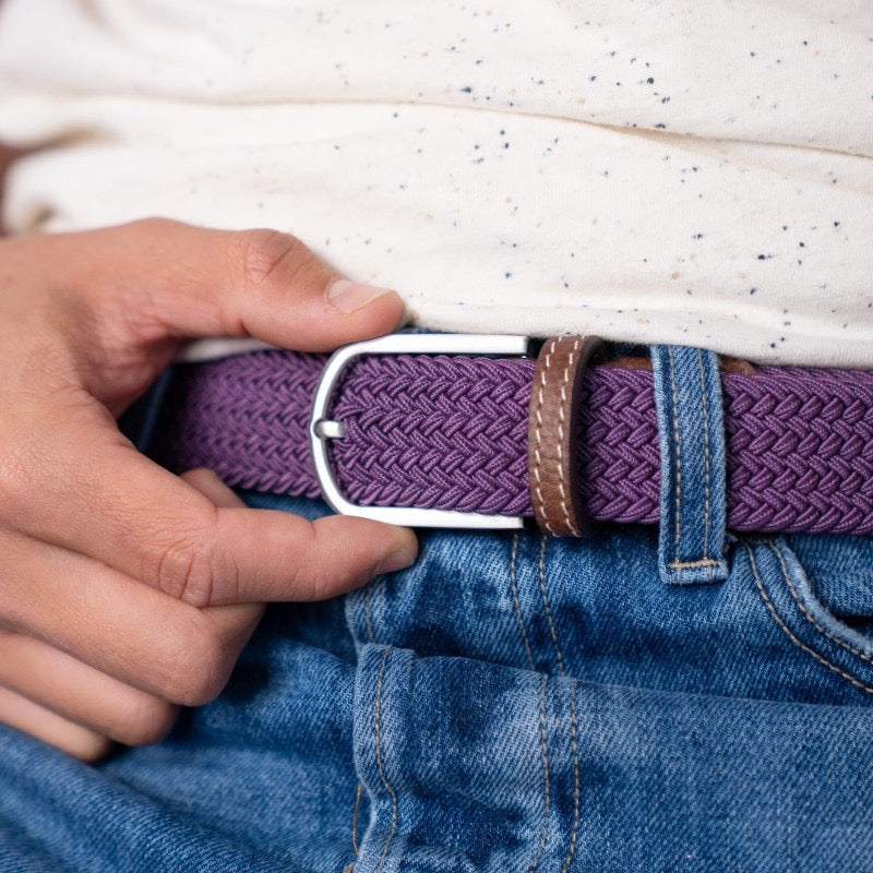 Person adjusting a plum belt on blue jeans with a white shirt.