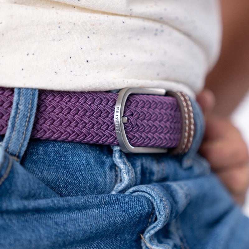Plum  belt with a silver buckle on blue jeans, worn by a person.